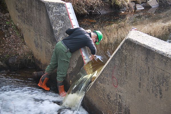 Un homme penché devant un petit barrage hydrographique pour prendre des mesures.