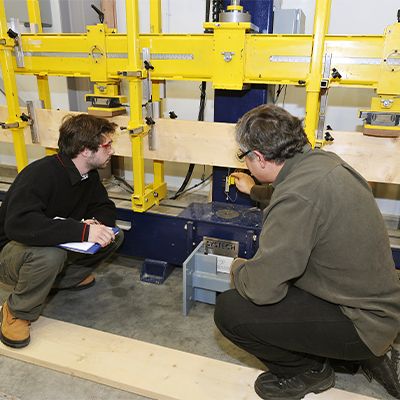 Un étudiant et un enseignant accroupis qui regardent une machine.