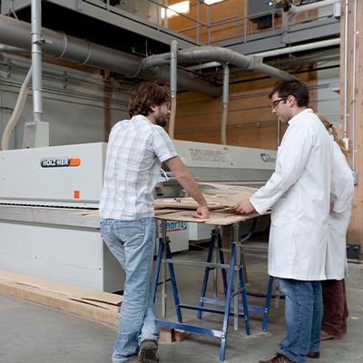 Un étudiant et un enseignant de dos qui discutent d'un projet près d'une machine.