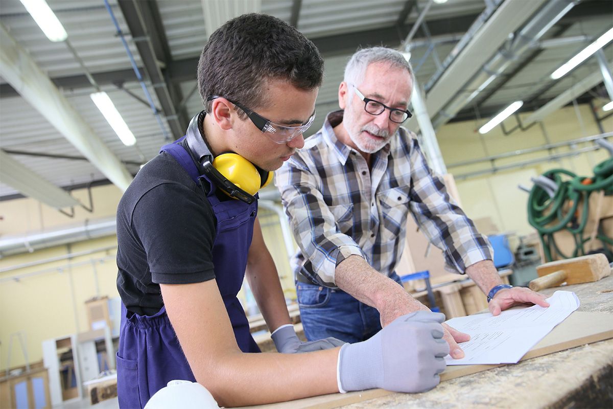 Un jeune homme et un travailleur sénior regardent un plan dans un atelier de bois