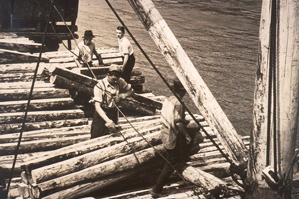 Image en noire et blanc d'hommes construisant un pont avec des billots de bois.