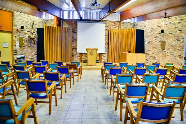 Auditorium montrant des chaises en bois en rangées devant un écran