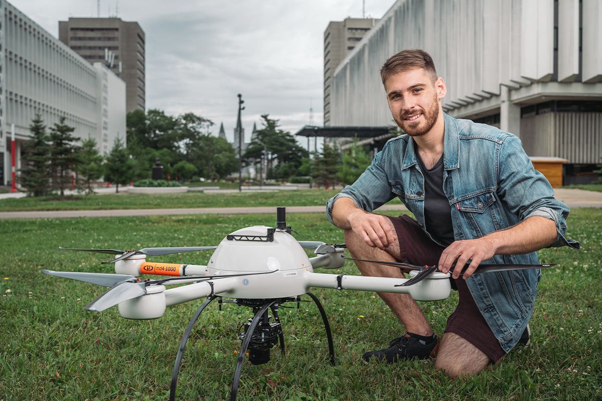 Baccalauréat en génie géomatique Jeune homme dehors accroupi près d'un drone