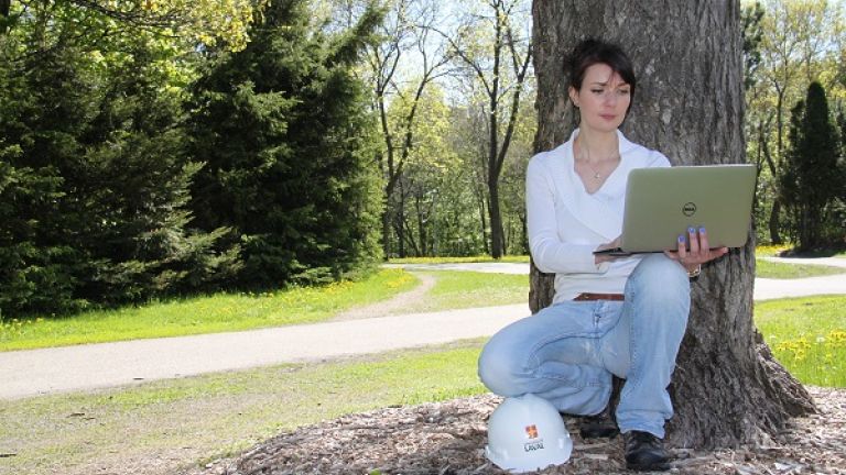 Étudiante en foresterie assise au pied d'un arbre avec un ordinateur